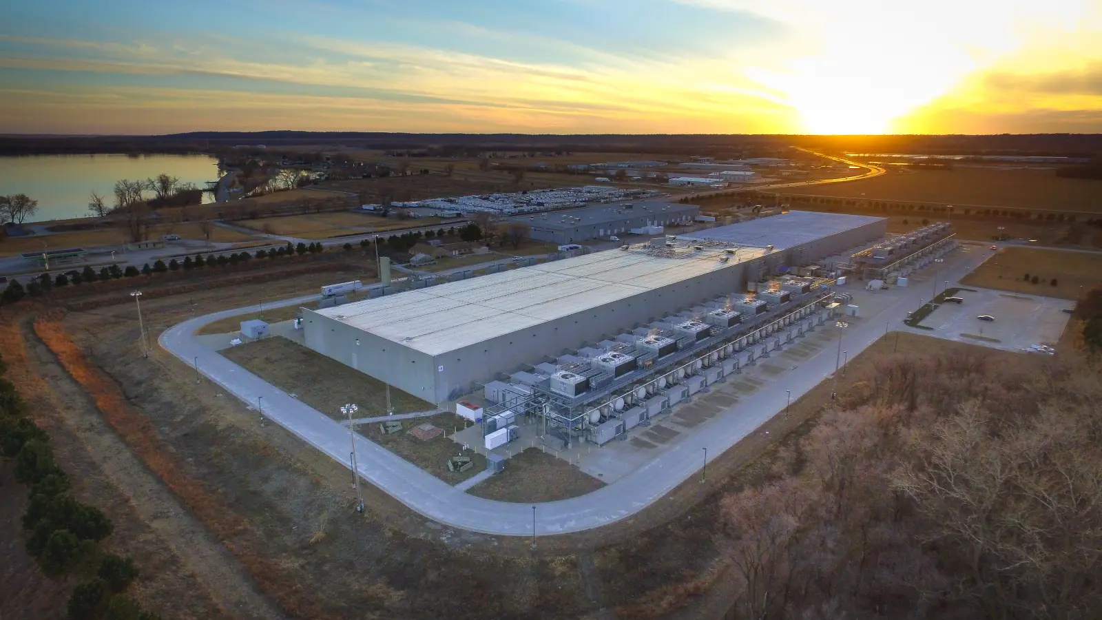 An aerial of a large data center building on open ground at sunset