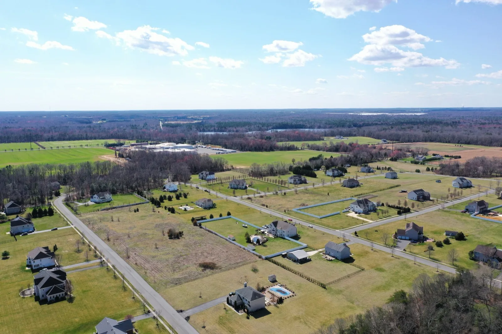 An aerial view of new single family homes on large lots among open fields and woods