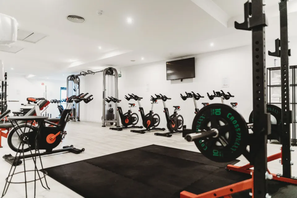 The floor of a fitness club, with cardio bikes and a weight rack
