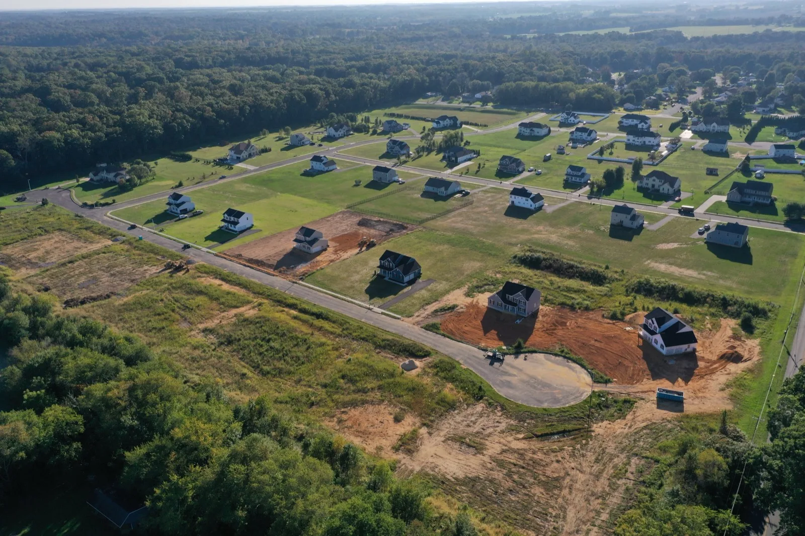 An aerial view of a new community being built, with finished houses, graded homesites and a curving new street among woods