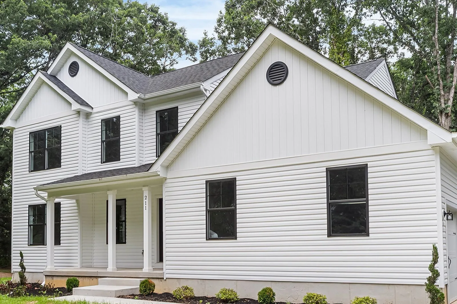 A newly built two story white home with black windows and fresh landscaping, with woods behind it, in Newfield
