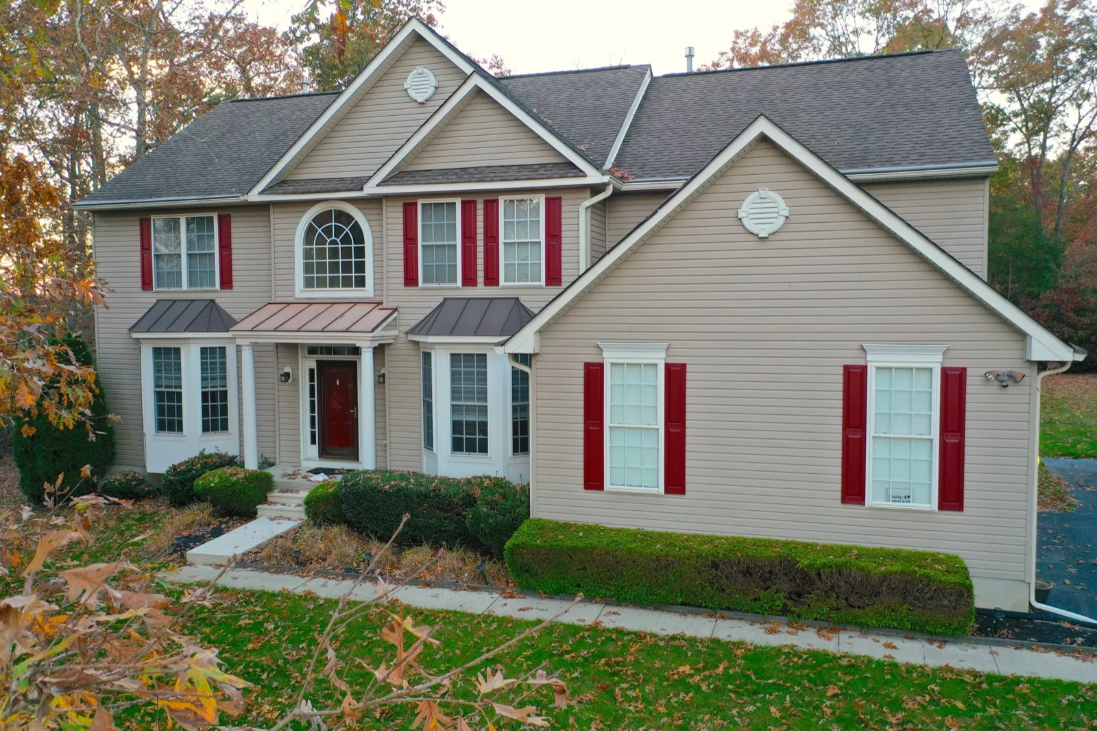 A two-story colonial home with red shutters and autumn leaves in front