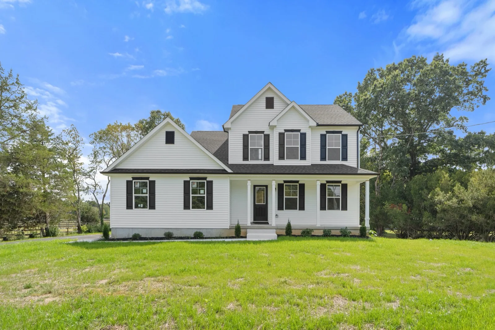 A newly built two-story white home with black shutters and a front porch on a green lawn
