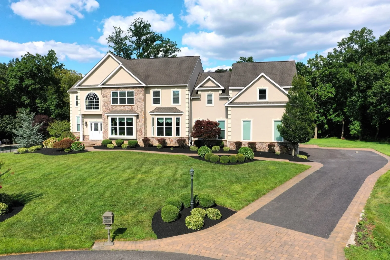 Two-story stone-front colonial home with a landscaped lawn and paver driveway in South Jersey