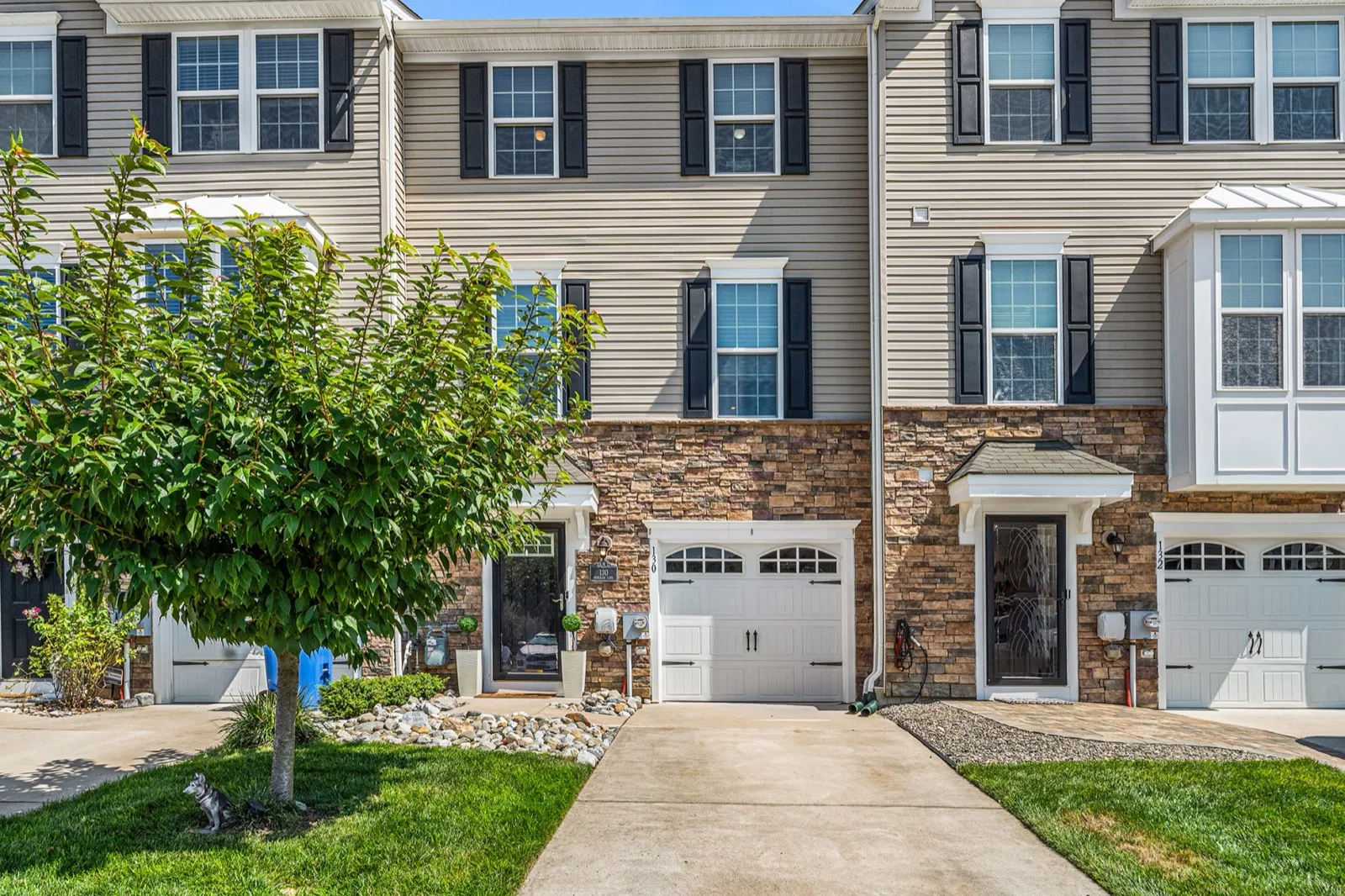 A row of two-story townhomes with stone fronts and single-car garages on a sunny day