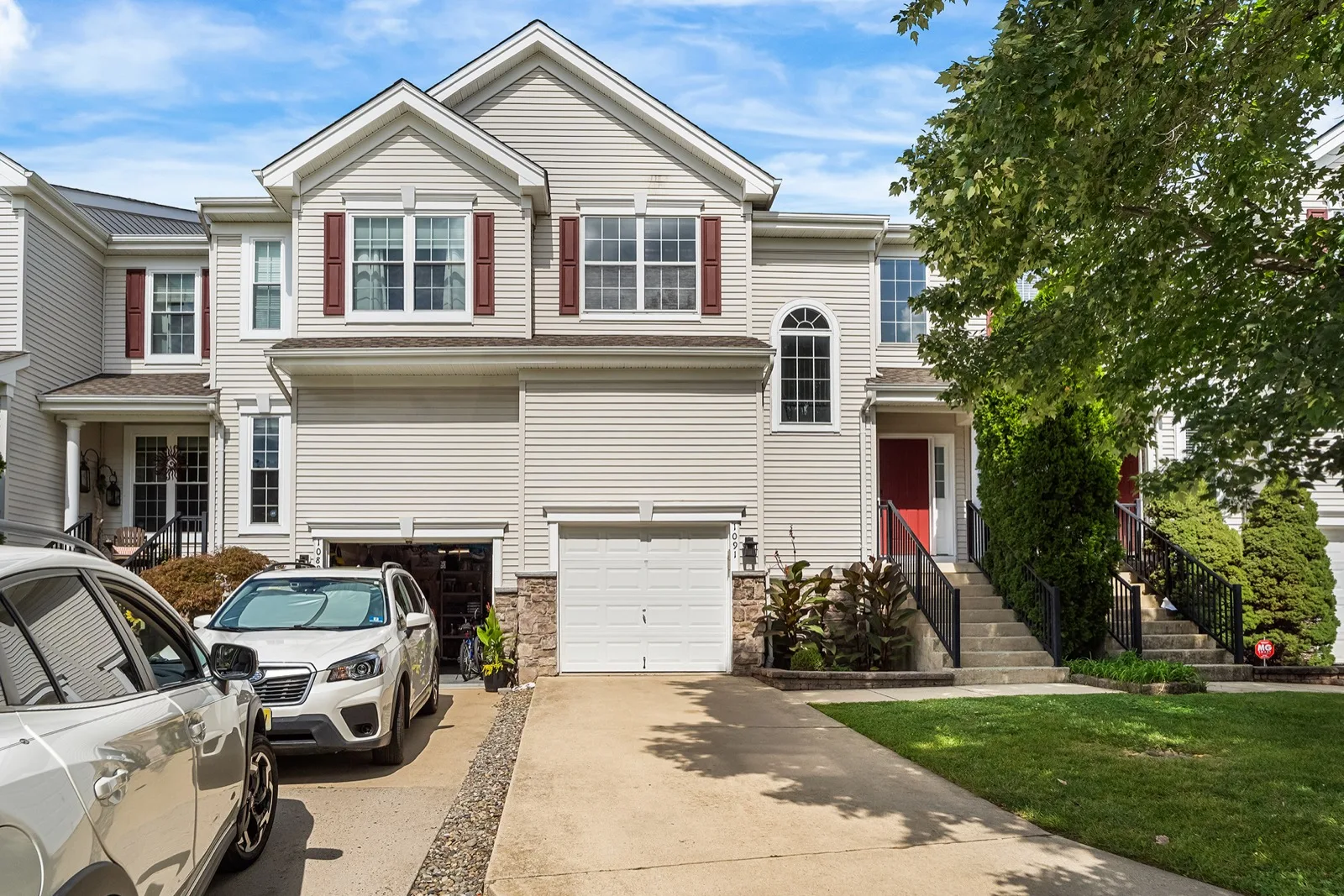 A two story attached townhome with a front garage, a driveway and steps up to a red front door